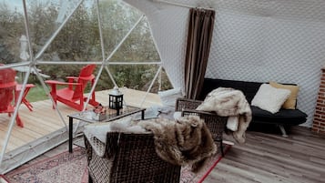 Un espace extérieur aménagé avec une tente, des meubles en osier, un canapé noir avec des coussins et une table rouge.