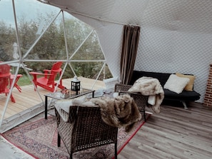 A tented outdoor area with wicker furniture, a black sofa with cushions, and a red table.