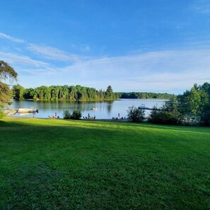 Un lago con barcos, una zona cubierta de hierba y árboles al fondo.