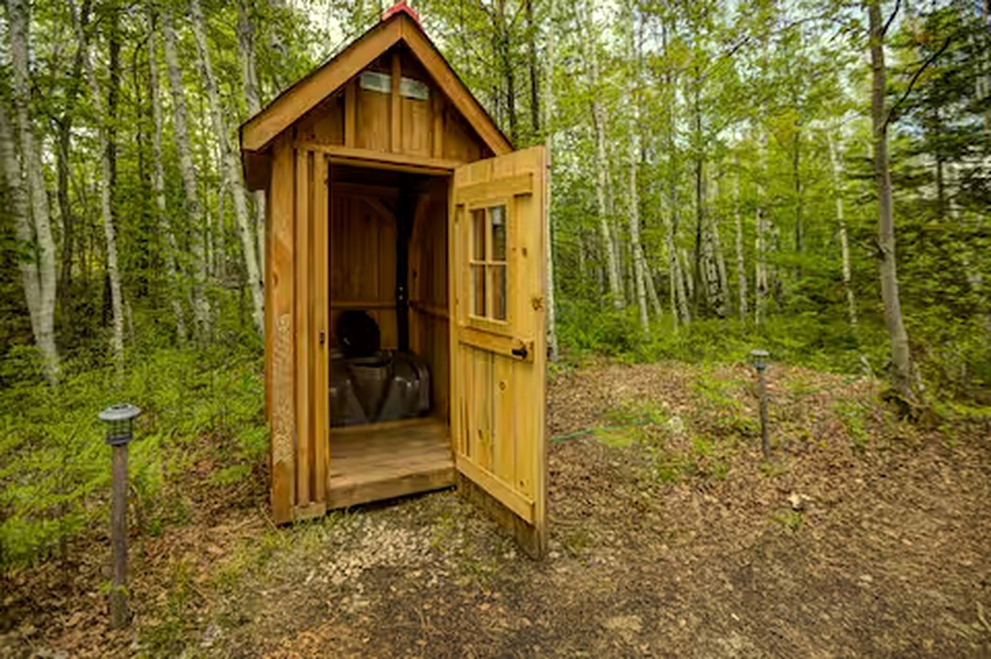 Une cabane en bois, avec la porte ouverte, entourée d’une forêt.