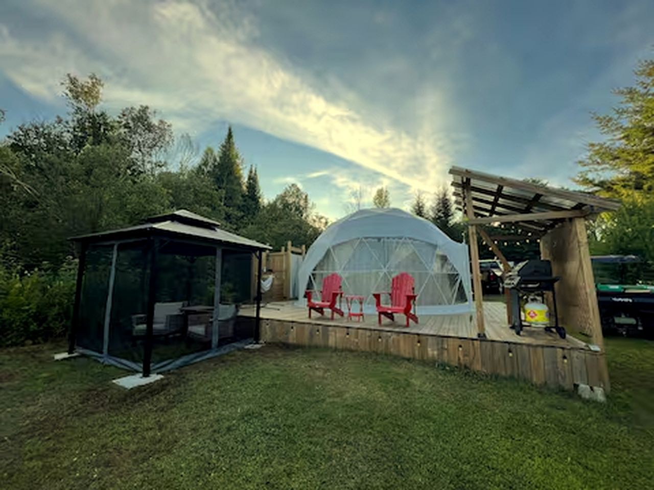 Un espace extérieur abrité, doté d’une structure en forme de dôme transparent, de chaises rouges et d’une terrasse en bois.