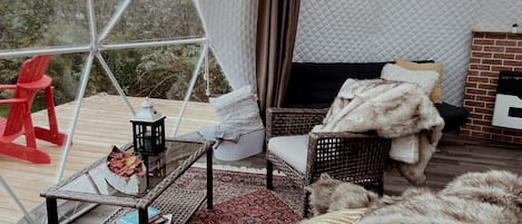 Un intérieur chaleureux avec un canapé en osier, une petite table surmontée d’une lanterne et une cheminée.