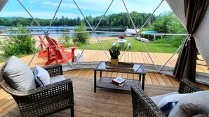Una habitación acogedora con muebles de mimbre, vistas a un lago y una terraza con mobiliario exterior.