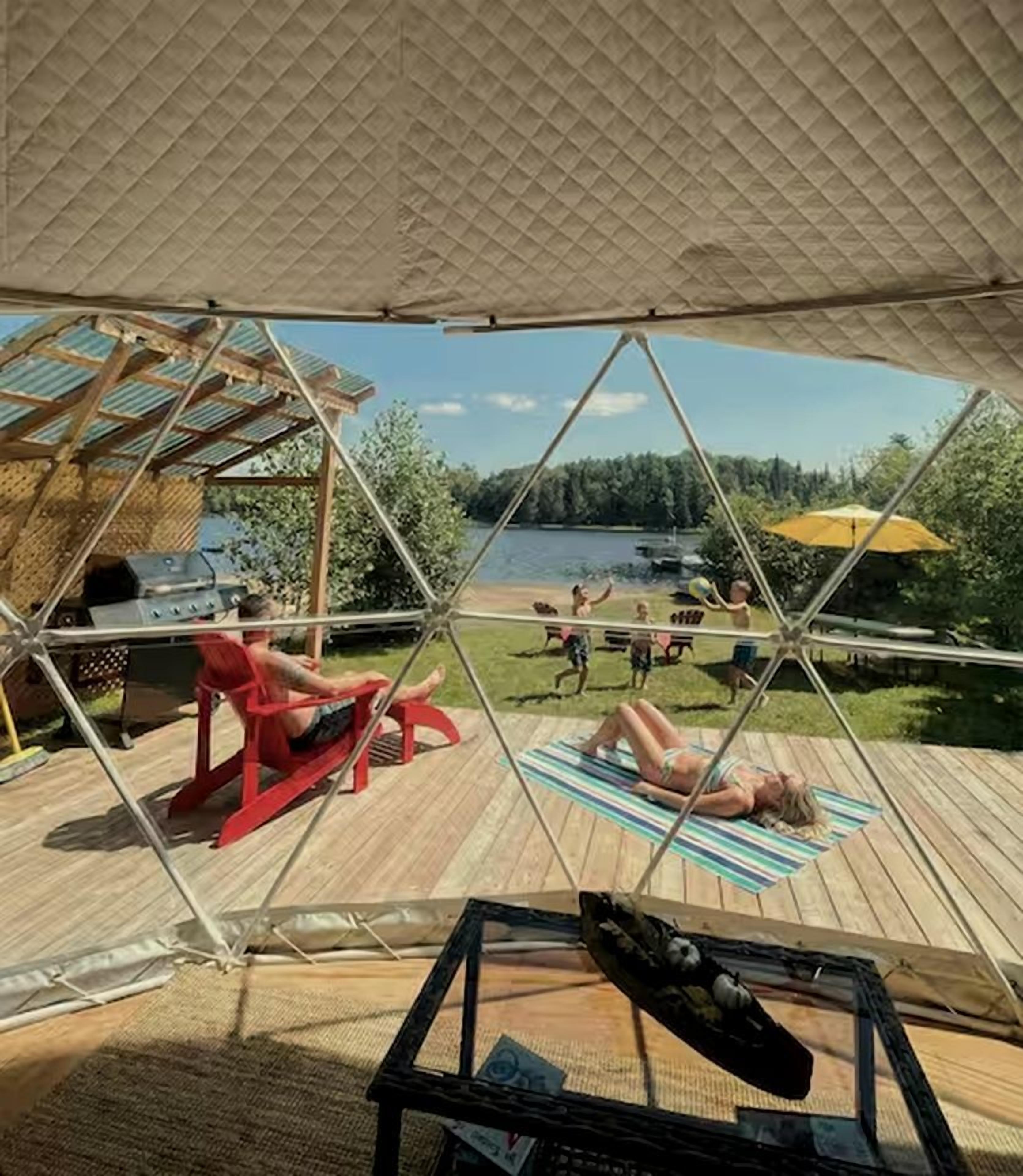 A covered outdoor area with a view of a lake, a barbecue grill, and people relaxing.