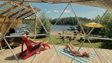 A covered outdoor area with a view of a lake, a barbecue grill, and people relaxing.