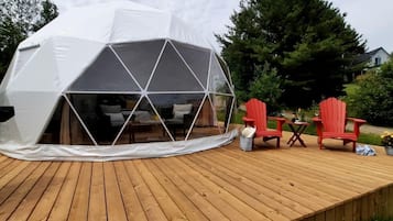 A geodesic dome structure with a wooden deck and red Adirondack chairs.
