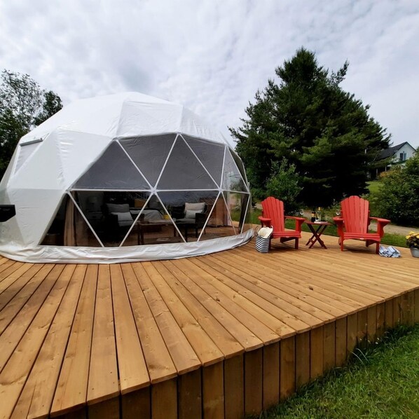 Una estructura de domo geodésico con un muelle de madera y sillas Adirondack rojas.