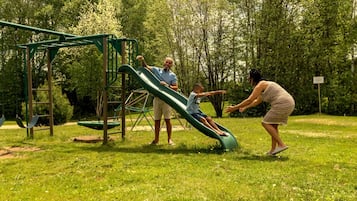 A playground with a slide and swings, surrounded by trees.