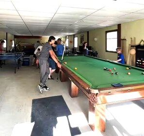 A billiards table in a room with other pool tables, chairs, and a window.