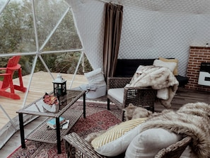 A cozy interior with a wicker sofa, a small table with a lantern, and a fireplace.