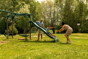 Een speeltuin met een glijbaan en schommels, omringd door bomen.