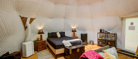 Una habitación acogedora y bien iluminada con una cama, lámparas de noche, una mesita, un banco y un sofá.