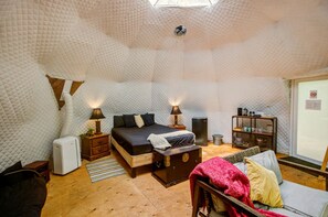 Una habitación acogedora y bien iluminada con una cama, lámparas de noche, una mesita, un banco y un sofá.