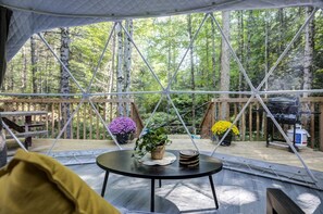 A tent with a round table, surrounded by a wooden deck, with a forest view.