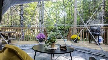 A tent with a round table, surrounded by a wooden deck, with a forest view.