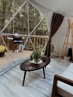 Et telt med geometrisk struktur, et rundt bord med en plante og en staffeli af træ.