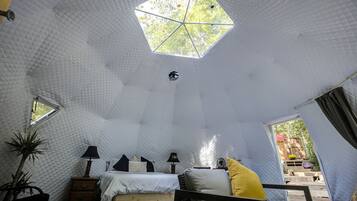 Une pièce avec un plafond aux motifs géométriques, un lit avec des oreillers, une chaise, une table de chevet et une fenêtre.