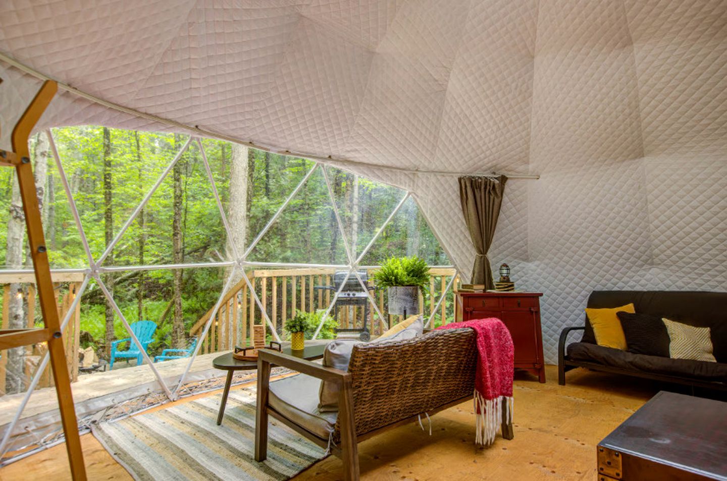 Un intérieur chaleureux avec une table en bois, des chaises, un canapé et une vue sur une forêt, visible à travers de grandes fenêtres.