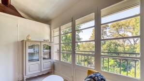 A room with a white cabinet, a small table, and large windows with a view of trees. - Guest Room 'La Sétoise' with Shared Terrace & Garden, Wi-Fi (Balaruc-le-Vieux)
