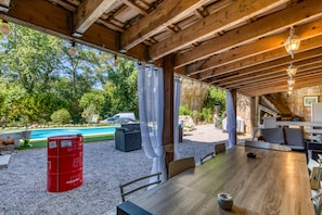 A covered outdoor dining area with a pool in the background.
