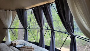 A tent-style bedroom with a bed, towels, and a view of greenery outside.