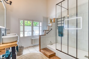 A modern bathroom with a large window, a bathtub, a shower enclosure, and a wooden vanity.