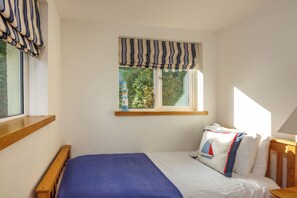 Un dormitorio con cama, cortinas en la ventana, una mesita de noche y una lámpara.
