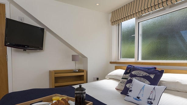 Ein Hotelzimmer mit Bett, Wand-Fernseher, Nachttisch aus Holz und Frühstückswagen auf dem Bett.