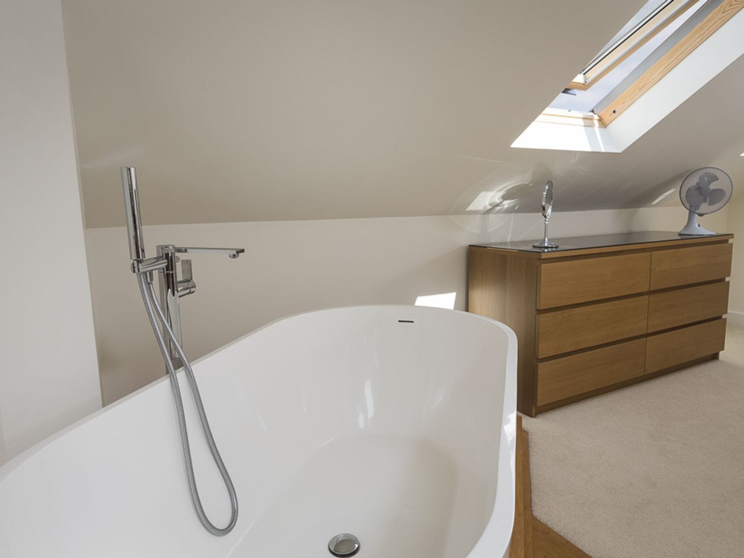 Een moderne badkamer met een vrijstaand bad, een houten wastafelmeubel en een dakraam.