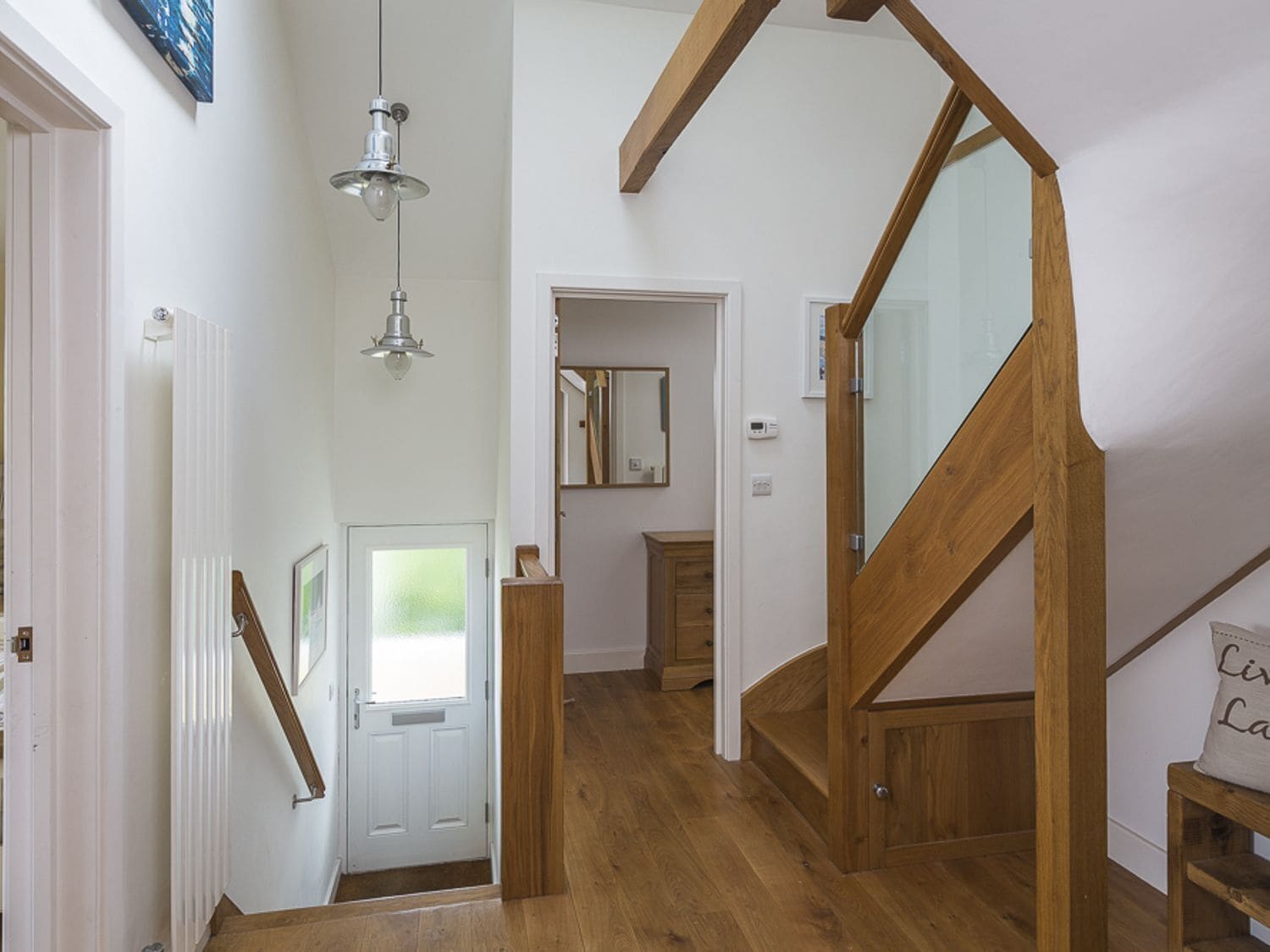 Eine Holztreppe mit Glastrennwand, eine weiße Tür mit Satinscheiben und eine Pendelleuchte.