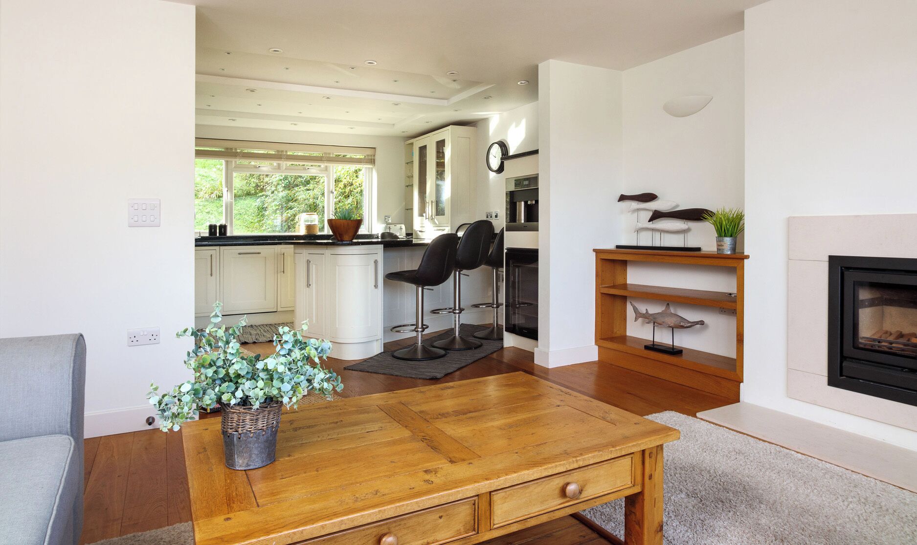 Una cocina moderna con armarios blancos, un comedor con mesa de madera y una chimenea.