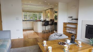 Una cocina moderna con armarios blancos, un comedor con mesa de madera y una sala de estar con sofá y chimenea.