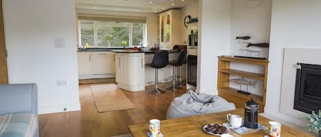 Una cocina moderna con armarios blancos, un comedor con mesa de madera y una sala de estar con sofá y chimenea.
