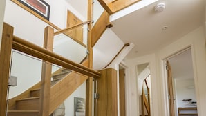Eine Holztreppe mit Glastrennungen, ein Flur mit Teppich und ein Blick in ein weiteres Zimmer mit einem Bett und Regalen.