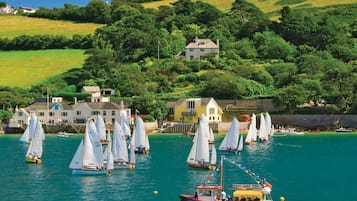A coastal scene with sailboats, a ferry, and houses on a hillside.