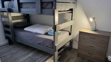 A bunk bed with a wooden frame, a bedside table with drawers, and a patterned rug on the floor.