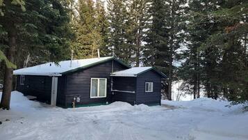 A cabin with a snow-covered roof, surrounded by evergreen trees.