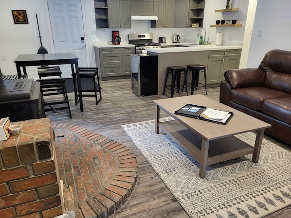 A living room with a fireplace, a coffee table, a couch, and a kitchen area in the background.