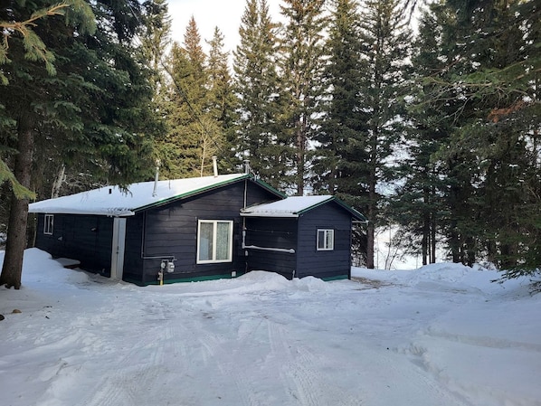 A cabin with a snow-covered roof, surrounded by evergreen trees.