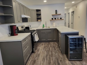A compact kitchen with grey cabinets, a stove, a sink, and a refrigerator.