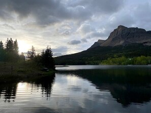 A calm lake with a mountain in the background and trees on the left.