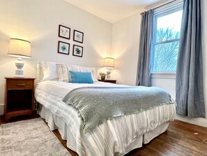 A bedroom with a bed, bedside lamps, a window with curtains, and wall art.