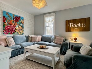 A living room with a sectional sofa, a coffee table, a painting, and a sign that says 'Brights'. - Beautiful, Rustic, Lodge with Pizza Oven, BBQ, and Porch for an Amazing Family Getaway in Ontario (South River)