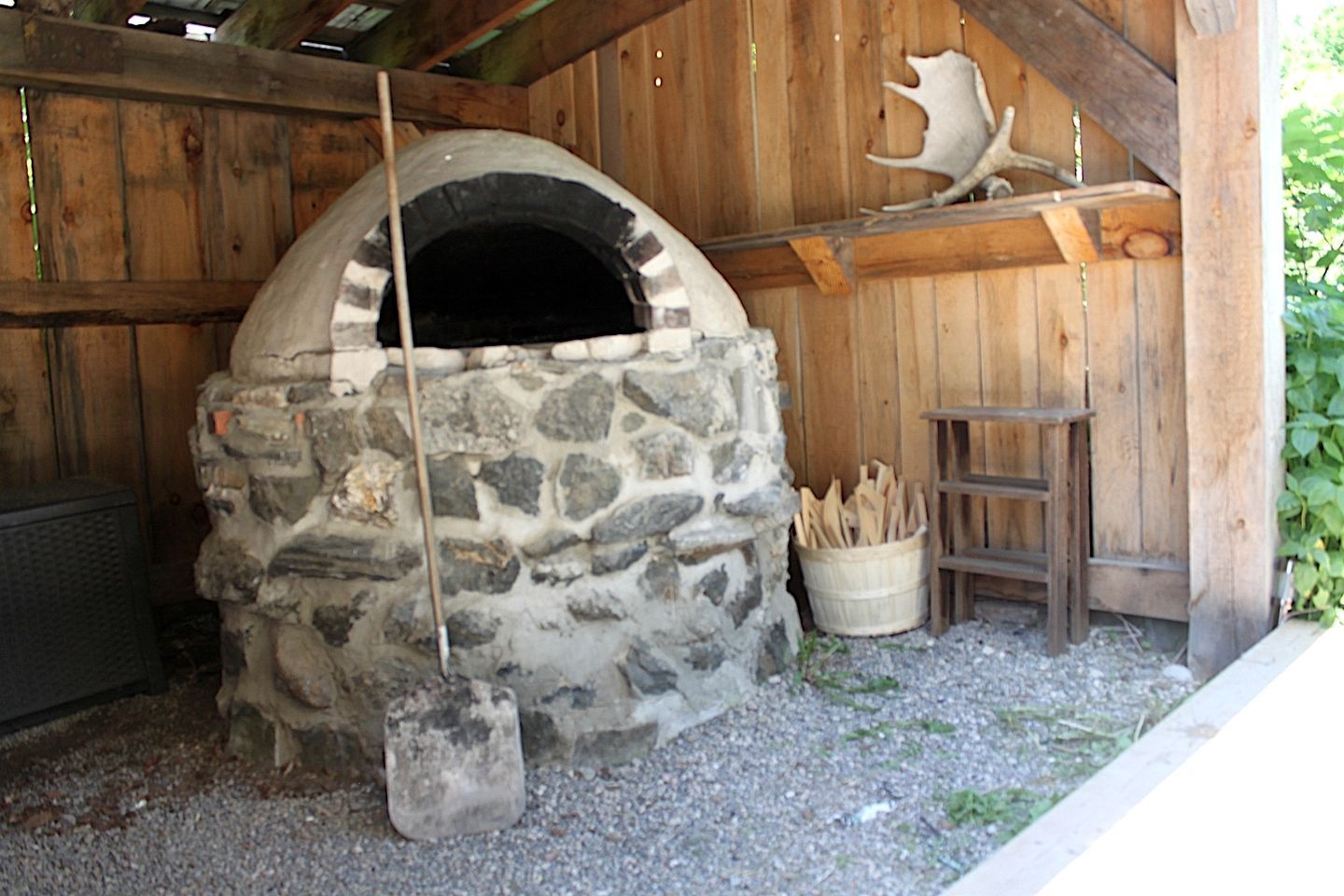 A stone-built outdoor oven with a wooden ladder and firewood nearby.