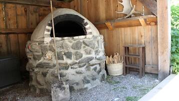 A stone-built outdoor oven with a wooden ladder and firewood nearby.