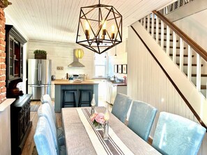 A modern kitchen with a dining area, a staircase, and a chandelier.