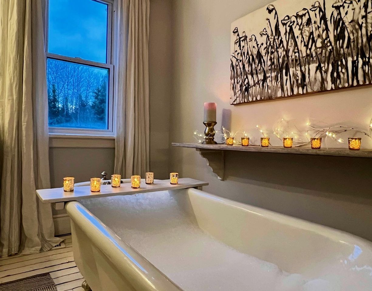 A bathroom with a bathtub, a window with curtains, and a shelf with candles.