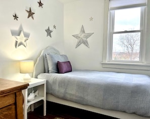 A bedroom with a bed, bedside table, lamp, and wall decorations.