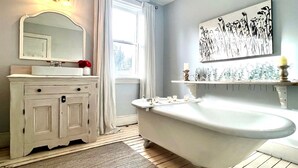 Un baño con una bañera independiente, un tocador con espejo y un estante en la pared.