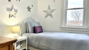 Een slaapkamer met een bed, nachtkastje, lamp en decoratie aan de muur.